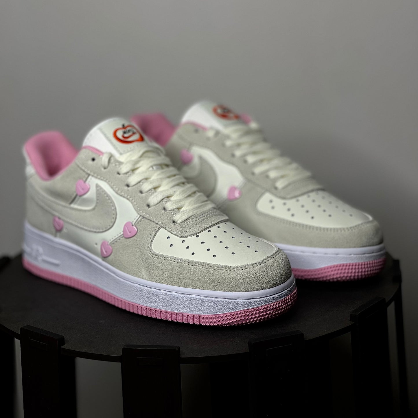 Pair of light gray and pink sneakers on a black surface with a neutral background