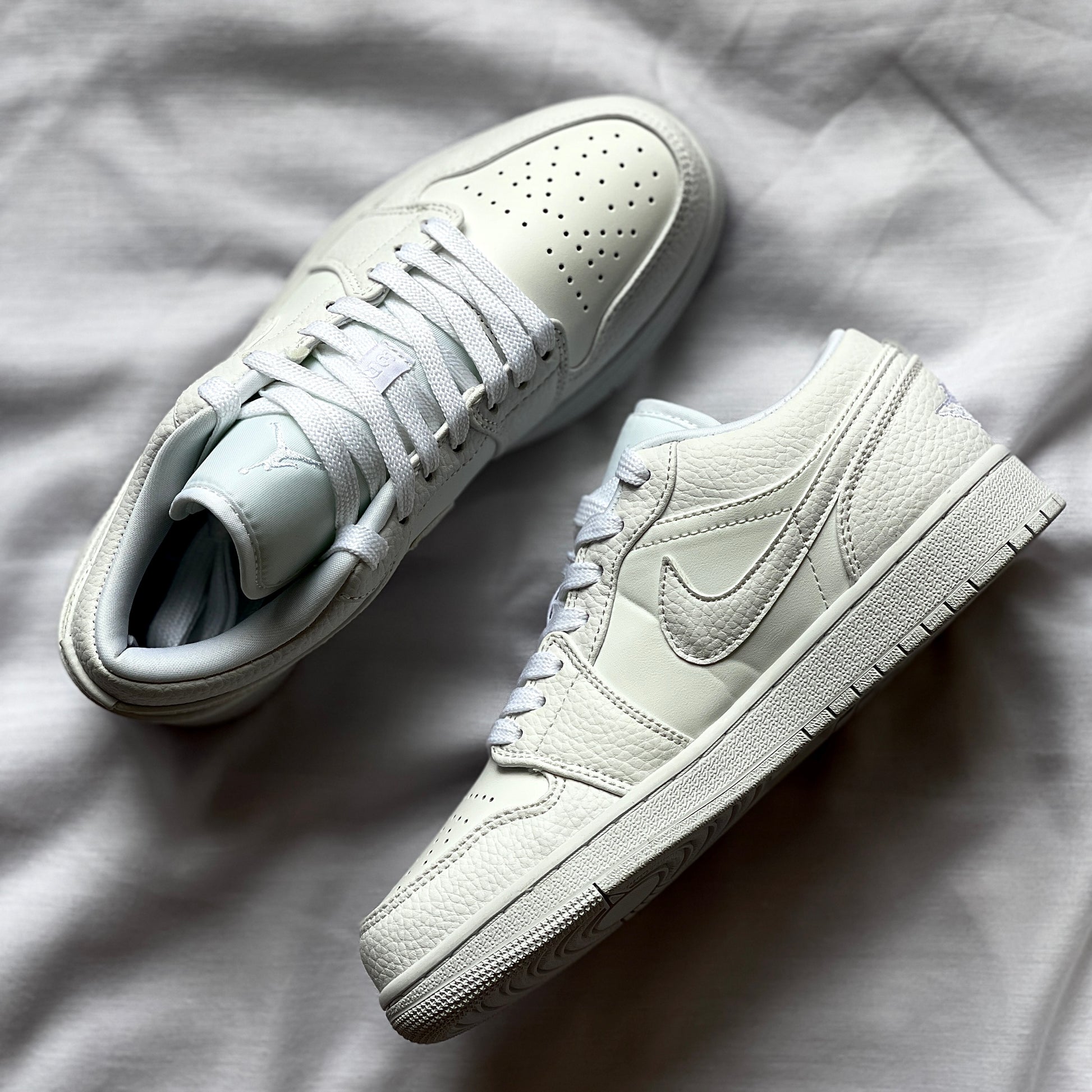 Close-up of Air Jordan 1 Low Triple White showing premium leather texture, stitching, and Air Jordan logo.