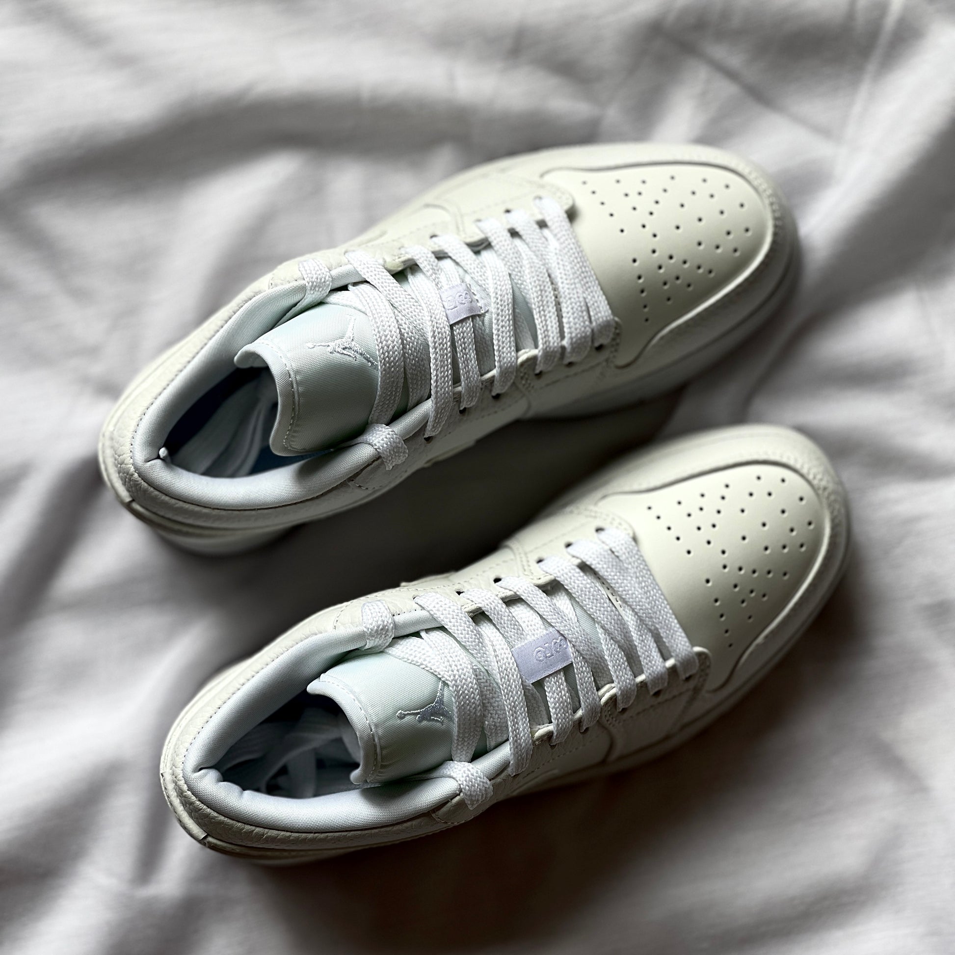 Top view of Air Jordan 1 Low Triple White highlighting laces, tongue, and smooth leather construction.