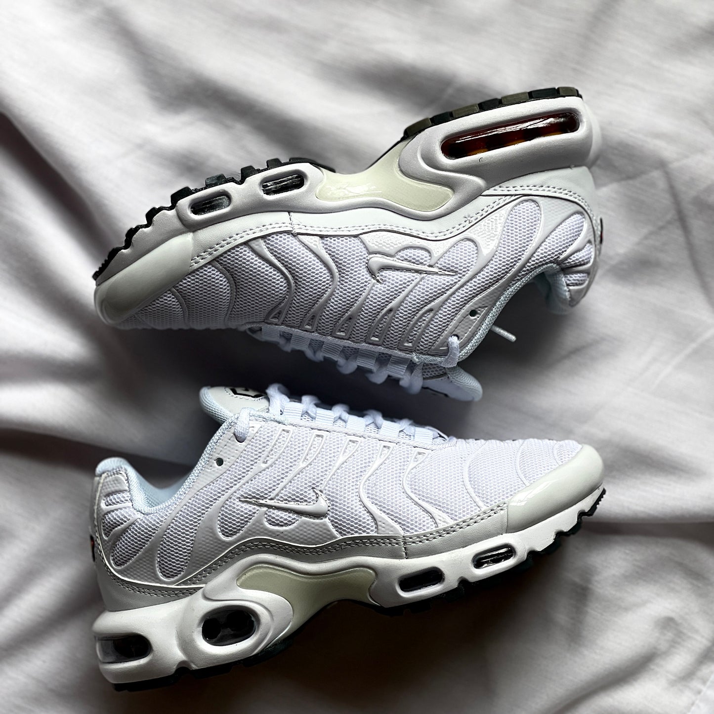 Side view of Nike Air Max Plus Triple White showing wavy upper design, Tuned Air midsole, and all-white colorway.