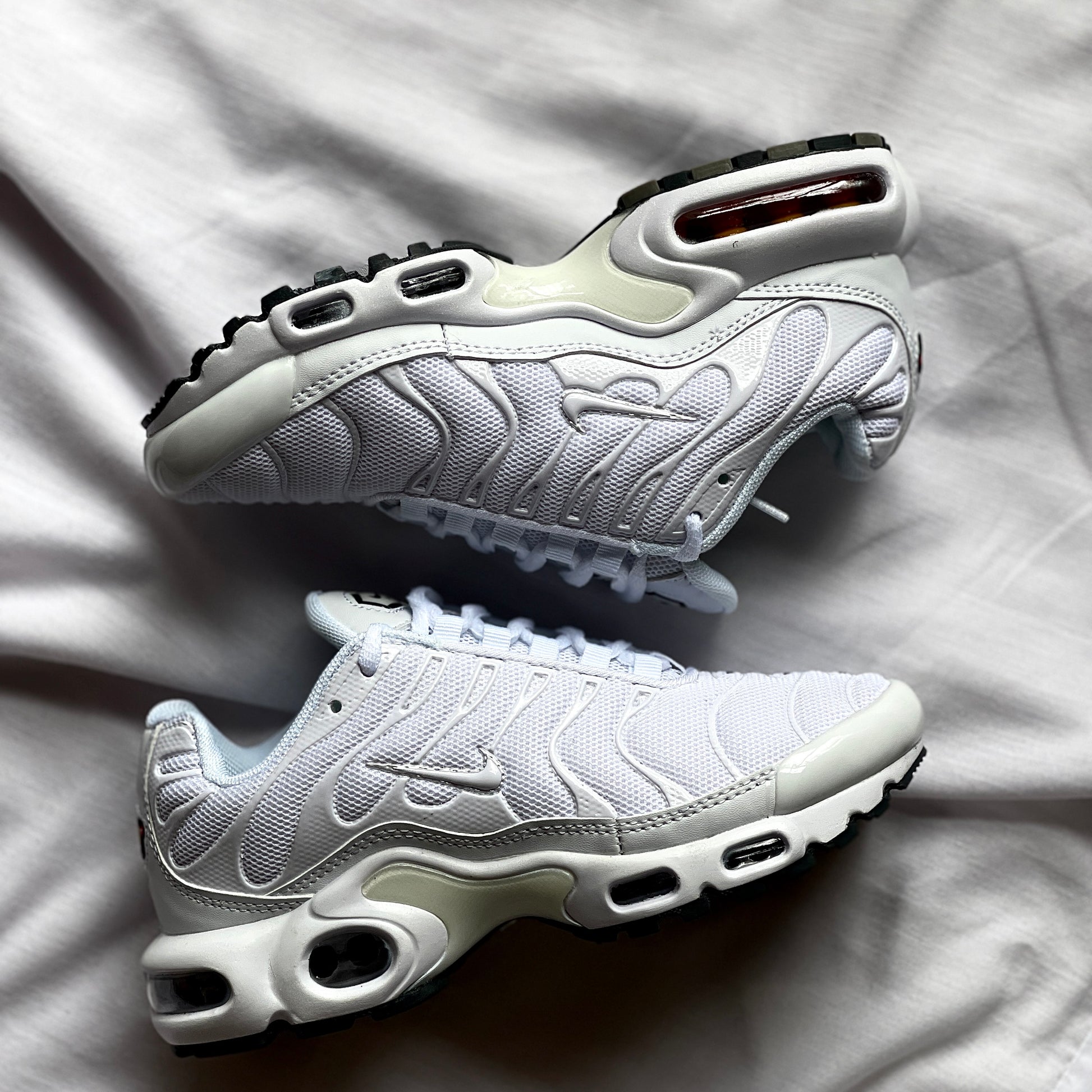 Side view of Nike Air Max Plus Triple White showing wavy upper design, Tuned Air midsole, and all-white colorway.