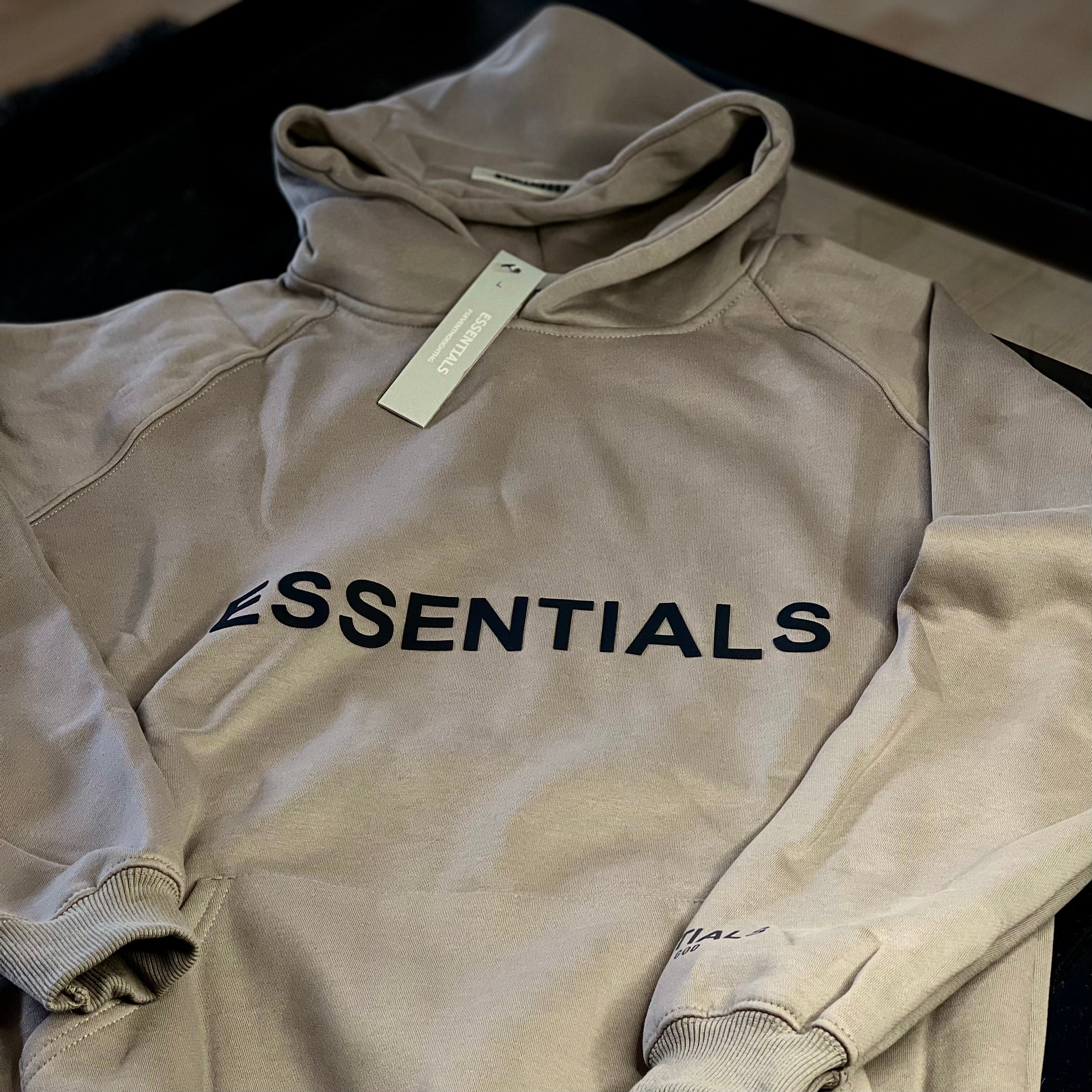 Close-up of Fear of God Essentials Hoodie Light Oatmeal fabric and logo patch — premium cotton-blend texture and subtle branding
