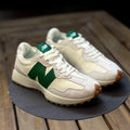 Pair of cream new balance 327 sneakers with green accents on a wooden surface