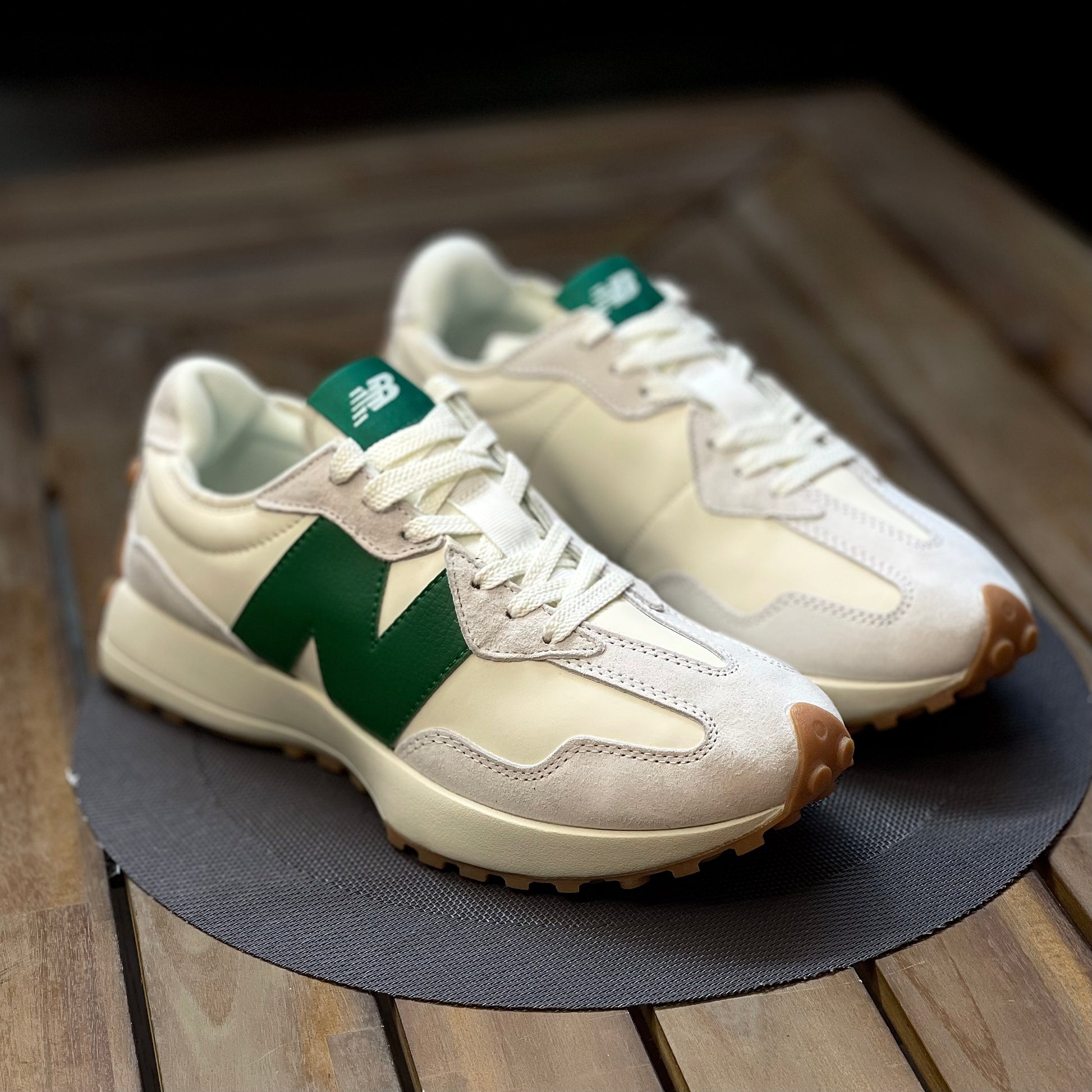 Pair of cream new balance 327 sneakers with green accents on a wooden surface