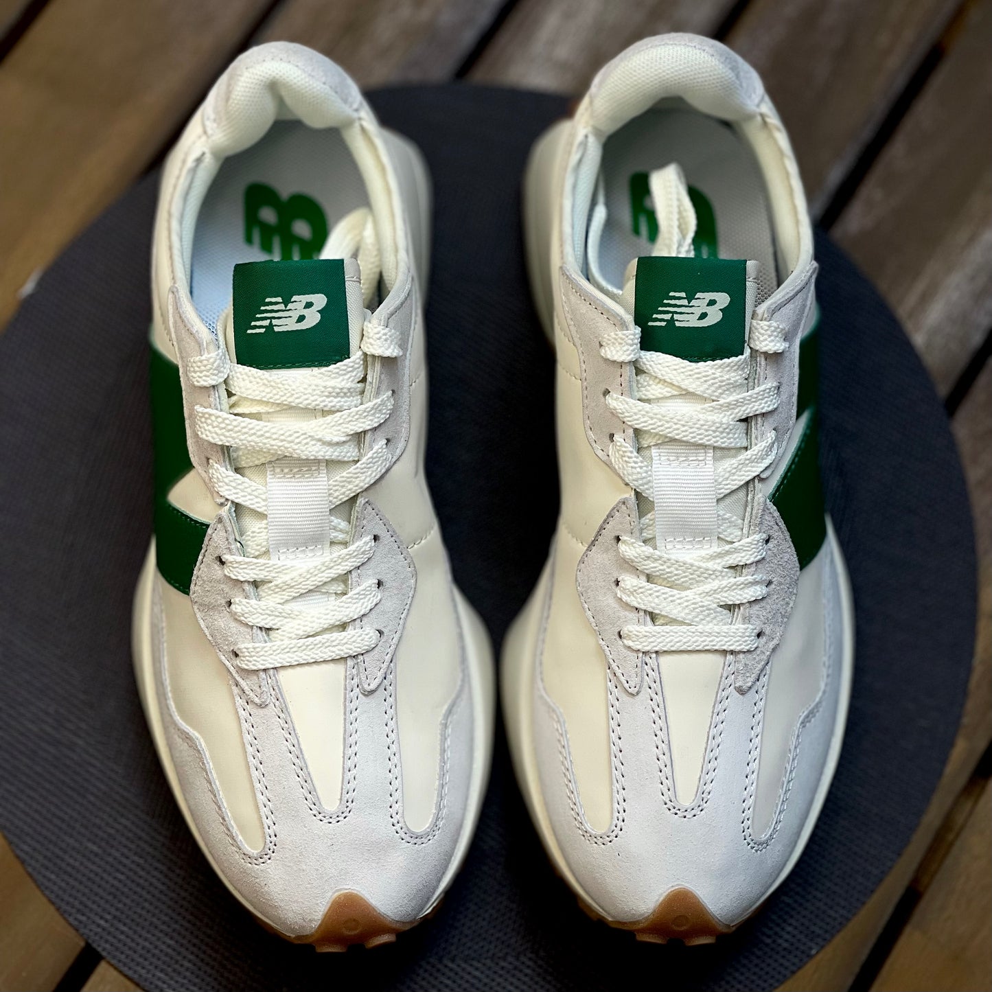 Pair of New Balance 327 cream-colored sneakers with green accents on a dark surface_3