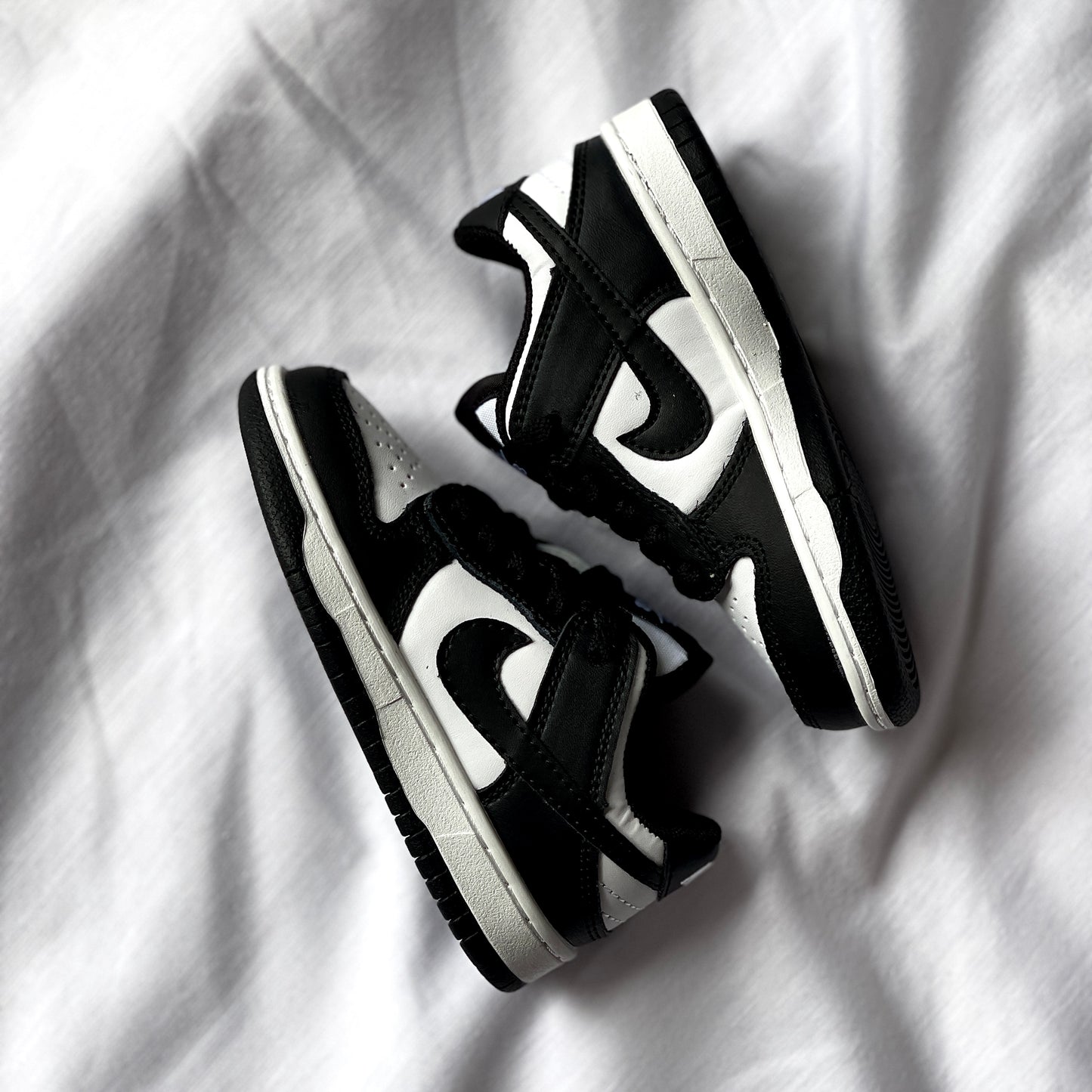 Side view of Nike Dunk Low Panda kids’ sneaker showing black overlays, white leather base, and low-top silhouette.