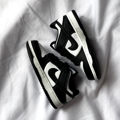 Side view of Nike Dunk Low Panda kids’ sneaker showing black overlays, white leather base, and low-top silhouette.