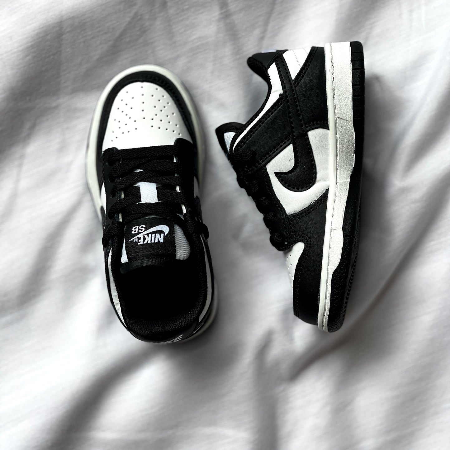 Close-up of Nike Dunk Low Panda kids’ sneaker showing leather texture, stitching, and black Swoosh logo.