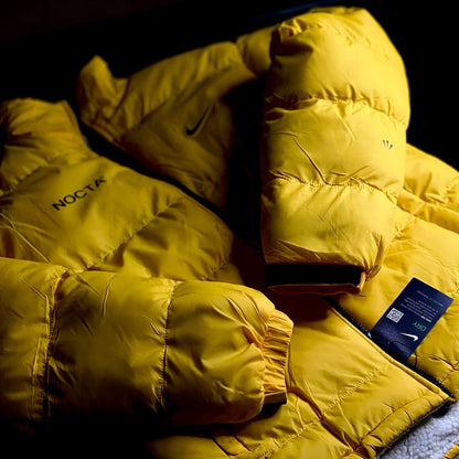 Close-up of Nike NOCTA Reversible Puffer Jacket showing University Gold outer shell and stitching detai